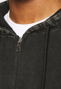 Felpa nera con zip e finitura testurizzata, con una cerniera e cordini argentati, progettata per comfort e calore.