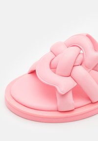 Gros plan d'une sandale rose avec une semelle coussinée et une épaisse sangle torsadée à l'avant.