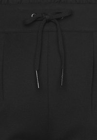 Calças de jogging pretas com cintura ajustável por cordão, pregas e textura de tecido suave. Inclui terminais de metal no cordão.