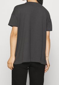 Tmavě šedé tričko s krátkým rukávem vyrobené z měkké bavlny se volným střihem, s kulatým výstřihem a viditelným švem podél lemu.