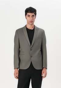 Blazer entallado de color verde oliva, hecho de una tela suave, con dos botones, un bolsillo en el pecho y dos bolsillos frontales con solapa.