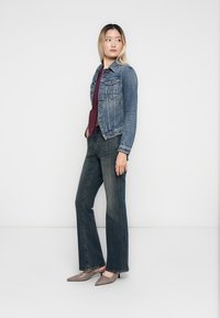 Jeansjakke i middels blå, med klassisk snitt, to frontlommer, kombinert med en burgunder topp og mørke flared jeans, komplementert med grå hæler.