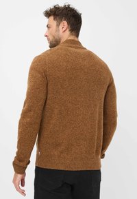 Pull en tricot marron avec un col montant, affichant une finition texturée et des poignets côtelés. Le design est classique et ajusté, avec un détail de marque subtil.