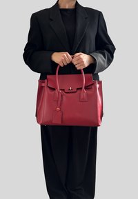 Czerwona skórzana torebka o strukturalnym wzorze, płaskim dnie, krótkich uchwytach i odpinanym metce. Noszona z czarną, oversize'ową marynarką.