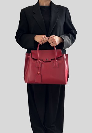 Červená kožená kabelka se strukturovaným designem, plochým vrcholem, krátkými uchy a odnímatelným štítkem. Nositá s černým oversized blejzrem.