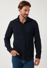 Cămașă navy cu mânecă lungă, din bumbac moale, având un guler clasic, placket frontal de lungime completă și un material texturat.