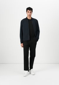 Jachetă bomber marină, tricou negru, pantaloni negri și adidași albi. Jacheta are fermoar și o croială lejeră, cu o textură de țesătură netedă.