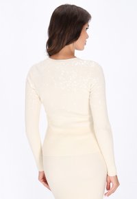 Rippstrick-creamfarbener Pullover mit langen Ärmeln, der auf der Rückseite mit verstreutem Paillettenbesatz für Textur und Detail verziert ist.