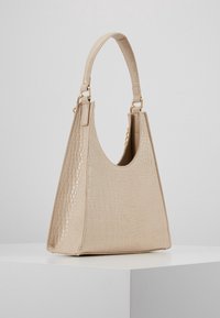 Beżowa torebka z tłoczeniem imitującym skórę krokodyla o trójkątnym kształcie, z krótkim uchwytem i złotymi elementami ozdobnymi. Gładka faktura, sztywna podstawa.