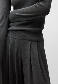 Maglione grigio scuro e gonna plissettata, realizzati in morbido tessuto knit, con una parte superiore aderente e una sezione inferiore fluida per una silhouette versatile.