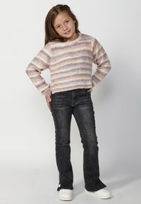 Pull rayé multicolore dans des teintes pastel, avec un col rond et des manches longues, associé à un jean évasé en denim foncé et des chaussures blanches.