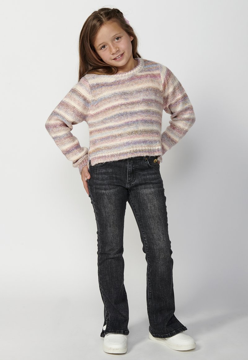 Pull rayé multicolore dans des teintes pastel, avec un col rond et des manches longues, associé à un jean évasé en denim foncé et des chaussures blanches.