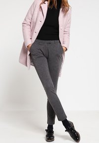 Jasnoróżowy, fakturowany płaszcz na czarnym golfie, szare, dopasowane spodnie i błyszczące czarne buty z akcentami w postaci kokardek. Prosty i elegancki design.