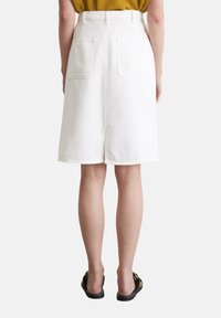Jupe midi en denim blanc avec une taille ajustée et deux poches arrière, dotée d'une fente au centre à l'arrière et d'une texture lisse, associée à des sandales noires.