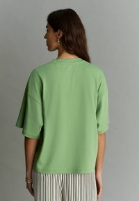 Top de manga corta y corte relajado en algodón verde claro con escote acanalado y hombros caídos, combinado con pantalones de pierna ancha a rayas.