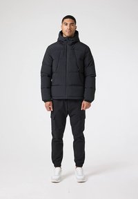 Black insulated puffer jacket with a hood, front zip closure, and two pockets, paired with black cargo pants and white sneakers.