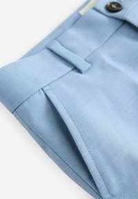 Svijetloplava haljina hlače od glatkog, teksturiranog materijala. Ima pojas s petljama za remen, dugme i detalj s jednim nabora.