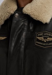 Chaqueta de cuero negra con un acolchado de piel de oveja tamizado en color marrón, dos bolsillos frontales y un parche bordado de PME Legend en el pecho.