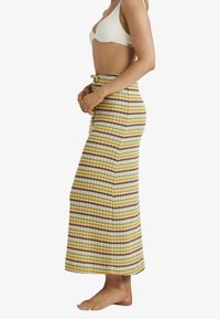 Gestreepte maxi rok in geel, groen en bruin met een gestructureerde stof, hoge taille en trekkoordsluiting. De getailleerde pasvorm accentueert de vorm.