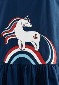 Marineblaues Kleid mit einem weißen Einhorn, das eine rot, blau und weiß gestreifte Mähne und einen Schwanz hat. Es steht auf einem Regenbogen mit einem Ankerdetail.