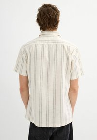 Camisa de manga corta con cuello en beige claro y finas rayas verticales grises. Tejido ligero con un dobladillo recto y un diseño de espalda liso.