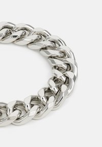 Collar de cadena de metal plateado con grandes eslabones entrelazados. El diseño presenta un acabado pulido y un aspecto grueso y resistente.