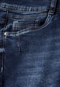 Un jean en denim bleu foncé présente une poche arrière visible avec des détails de couture, un bouton en métal et une texture lisse.