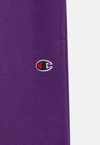 Ljubičasta pamučna tkanina s izvezenim logotipom u crvenoj i crnoj boji. Tekstura je glatka s blagim rastezanjem.