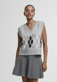 Gaiši pelēks adīts vestes ar V-veida kaklu, ar melnbaltu dimantu rakstu. Apvienota ar pelēku flared ribbed svārku.