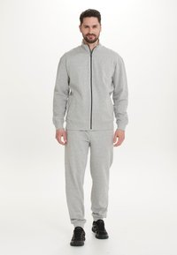 Grauer Reißverschluss-Hoodie mit Stehkragen, kombiniert mit passenden Hosen. Glatte Textur, gerippte Bündchen und schwarze Akzente am Reißverschluss. Schwarze Sportschuhe.