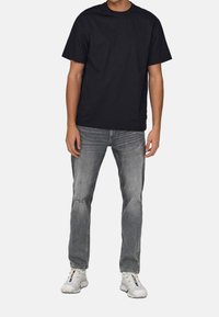 Schwarzes Baumwoll-T-Shirt mit Rundhalsausschnitt, kombiniert mit grauen, ausgebleichten Jeans und weißen Sneakers mit mehrfarbigen Akzenten.