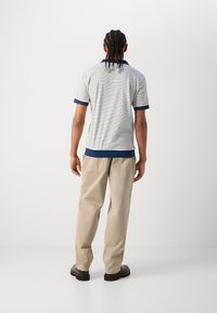 Chemise polo rayée en bleu marine et blanc, avec des manches courtes et un col côtelé, assortie à un pantalon beige clair et des chaussures noires.