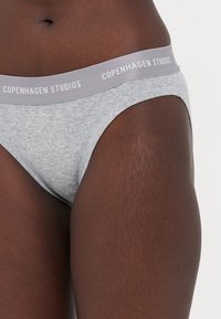 Slip gri din material pilos, cu o talie elastică lată etichetată "COPENHAGEN STUDIOS." Textură netedă și design aderent.