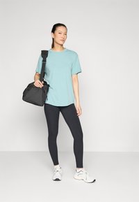 Lys blå kortermet t-skjorte, svarte leggings og hvite sneakers, med en svart gymbag hengende fra skulderen. Glatt stofftekstur.