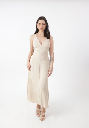 Abito maxi beige con scollatura a V profonda, corpetto aderente e gonna fluttuante. Tessuto leggero e morbido con una sottile texture, abbinato a tacchi a strappo.