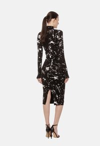 Czarna sukienka bodycon z białym abstrakcyjnym wzorem plam farby, z długimi rękawami, wysokim dekoltem, do kolan oraz rozcięciem z tyłu.