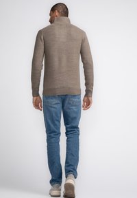 Pulover tricotat maro cu guler înalt, manșete și tiv cu model în dungi. Purtați peste blugi albaștri deschis și adidași bej. Design simplu, țesătură texturată.
