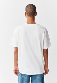 Tricou alb din bumbac, cu mâneci scurte, guler rotund și croială lejeră. Are o textură fină și un design curat, minimalist.