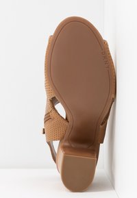 Sandale marron avec des brides perforées vue de la semelle, avec un talon carré et le logo DKNY sur la semelle.