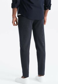 Pantaloni neri blu scuro, con una vestibilità su misura, caratterizzati da cuciture laterali e gambe affusolate, indossati con scarpe da ginnastica bianche.
