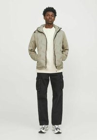 Lichtgrijze pufferjack met ritssluiting en capuchon, gecombineerd met een crèmekleurig sweatshirt en zwarte cargobroek. Bevat contrasterende zwarte accenten.