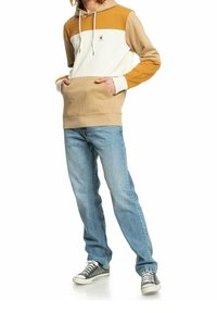 Felpa con cappuccio dal design a blocchi di colore in crema, senape e beige. Presenta una tasca a marsupio frontale e cappuccio con stringa. Indossata con jeans blu.