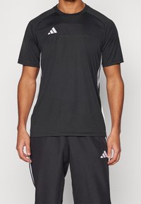 Svart idrottströja med korta ärmar, kontrasterande vita adidas-ränder på sidorna och en strukturerad panel på bröstet.