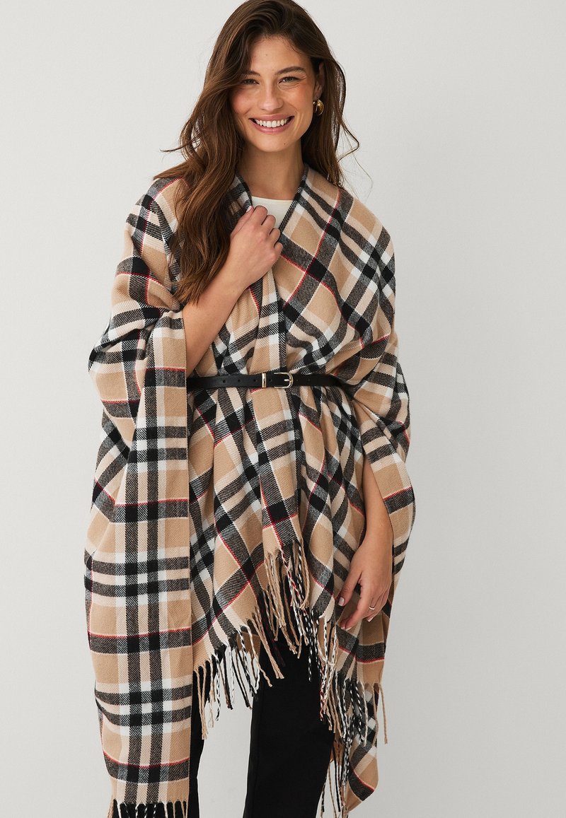 Beige and black plaid poncho with red accents, fringed hem, and belted design; made from soft, textured material.