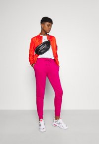 Lysorange bomberjacka, vit Nike t-shirt, rosa mjukisbyxor och svart midjeväska. Vita och grå sneakers med röda detaljer.
