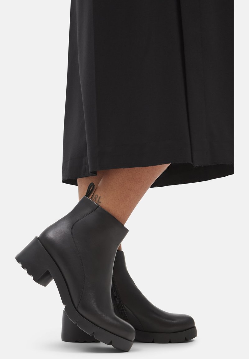 Botas de tobillo de cuero negro con un tacón grueso y estriado, y una cremallera lateral, que presentan una textura suave y un diseño moderno y elegante.