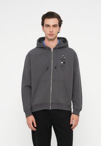 Ζακέτα με φερμουάρ σε σκούρο γκρι μείγμα βαμβακιού; διαθέτει μπροστινή τσέπη, ρυθμιζόμενη κουκούλα και τύπωμα λογότυπου στο στήθος.