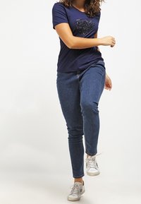Navy t-shirt with short sleeves, featuring a sequin heart design, paired with blue denim jeans and white sneakers. Simple and casual outfit.