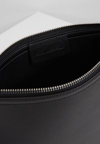 Černý kožený vnitřek kabelky s uzavíráním na zip a raženou značkovou štítkem. Hladká textura s matným povrchem. Stříbrné kování zipu.