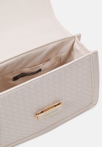 Cremefarbener gewebter Clutch mit glatter Oberfläche, goldfarbener Hardware und einem innenliegenden Markenetikett. Die Tasche verfügt über ein weiches Innenfutter und eine strukturierte Form.